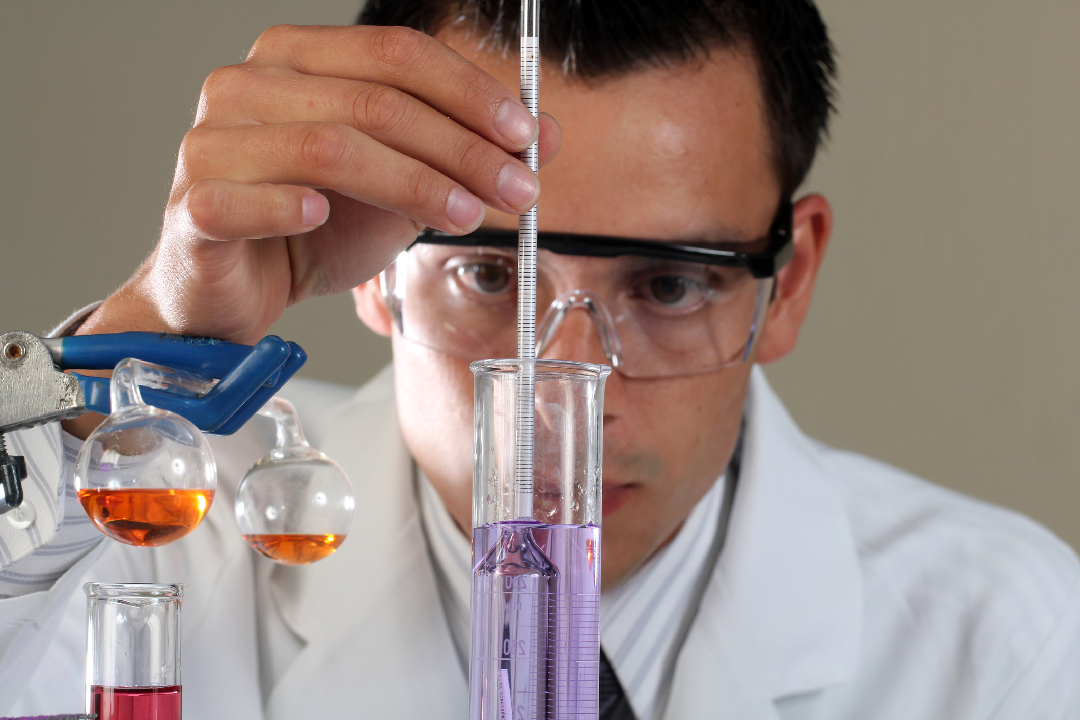 A scientist dipping a small cylindrical glass container into a purple solution.