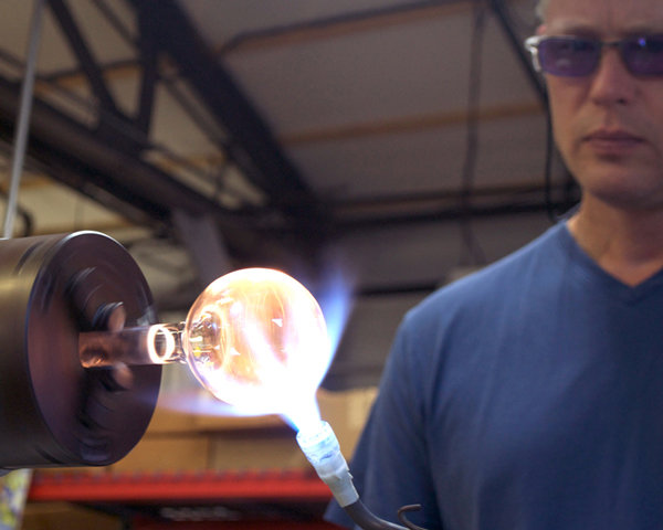 A man with goggles on heating glass under a blowtorch.