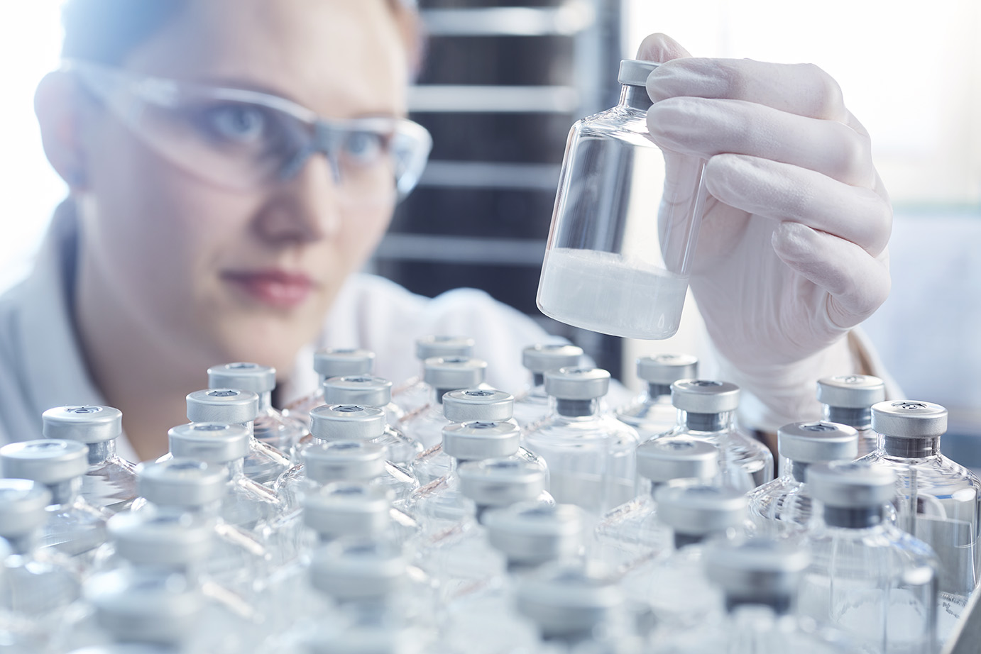 A scientist in a lab looking at a vial filled a third of the way full with a white powder.