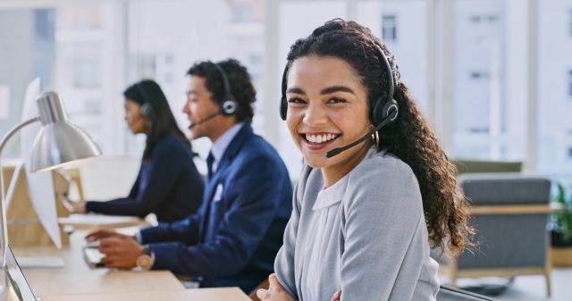 Woman with dark curly hair smiling at work with a headset on.