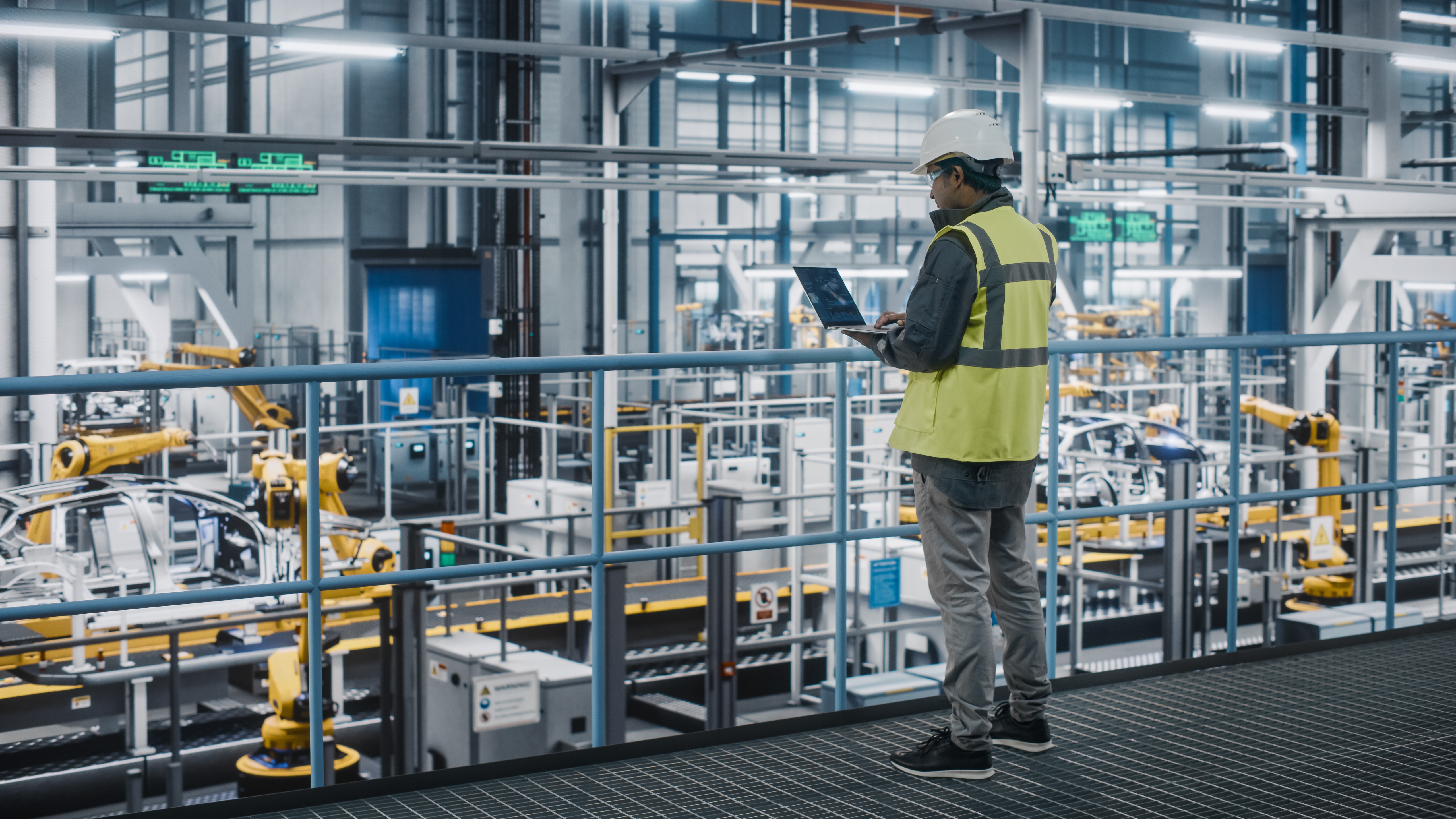 A man in a yellow jacket overseeing manufacturing in a factory.