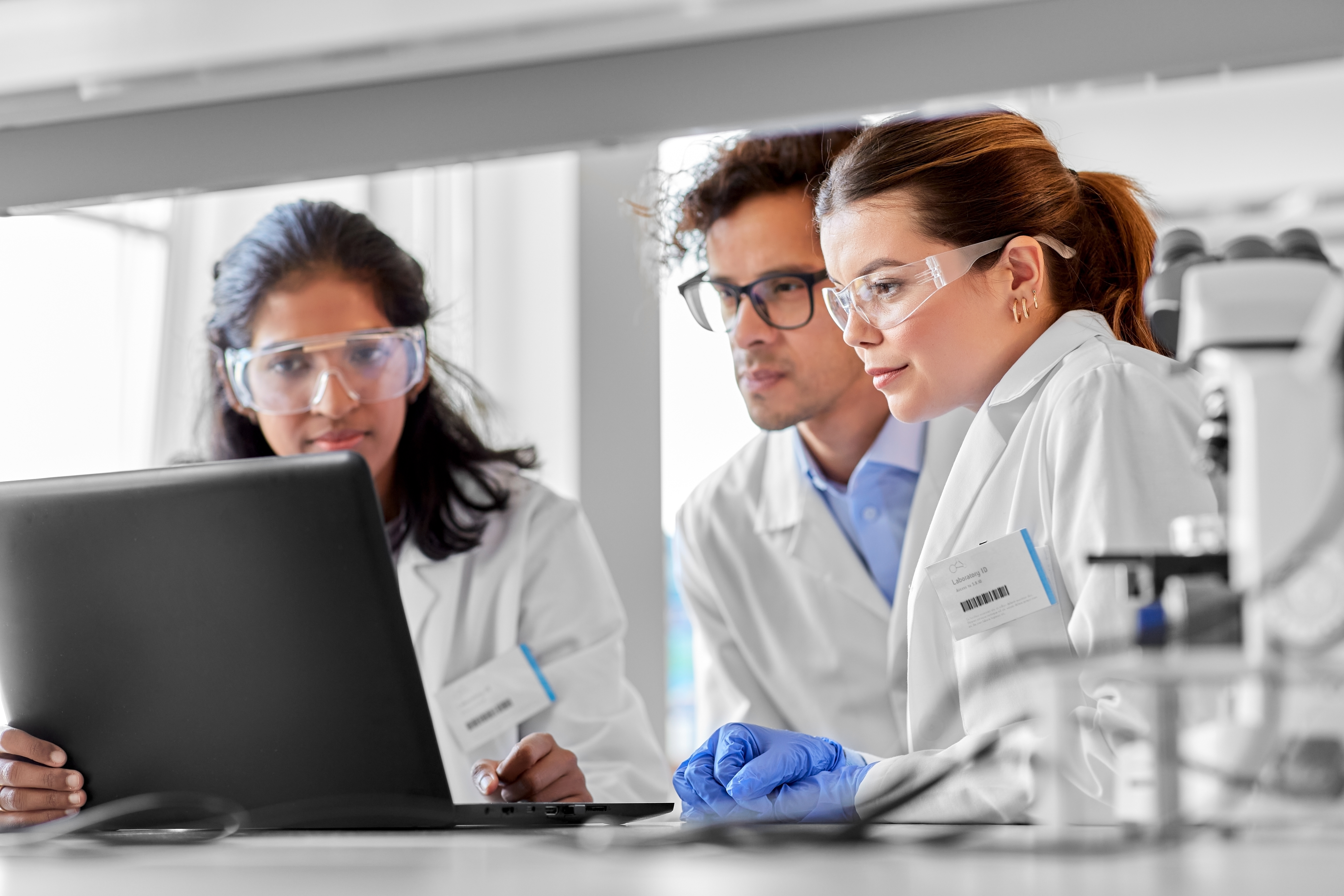 Three scientists in white coats looking at a laptop together.