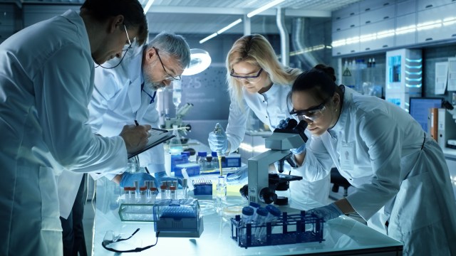 A group of scientists wearing white coats doing research in a lab.