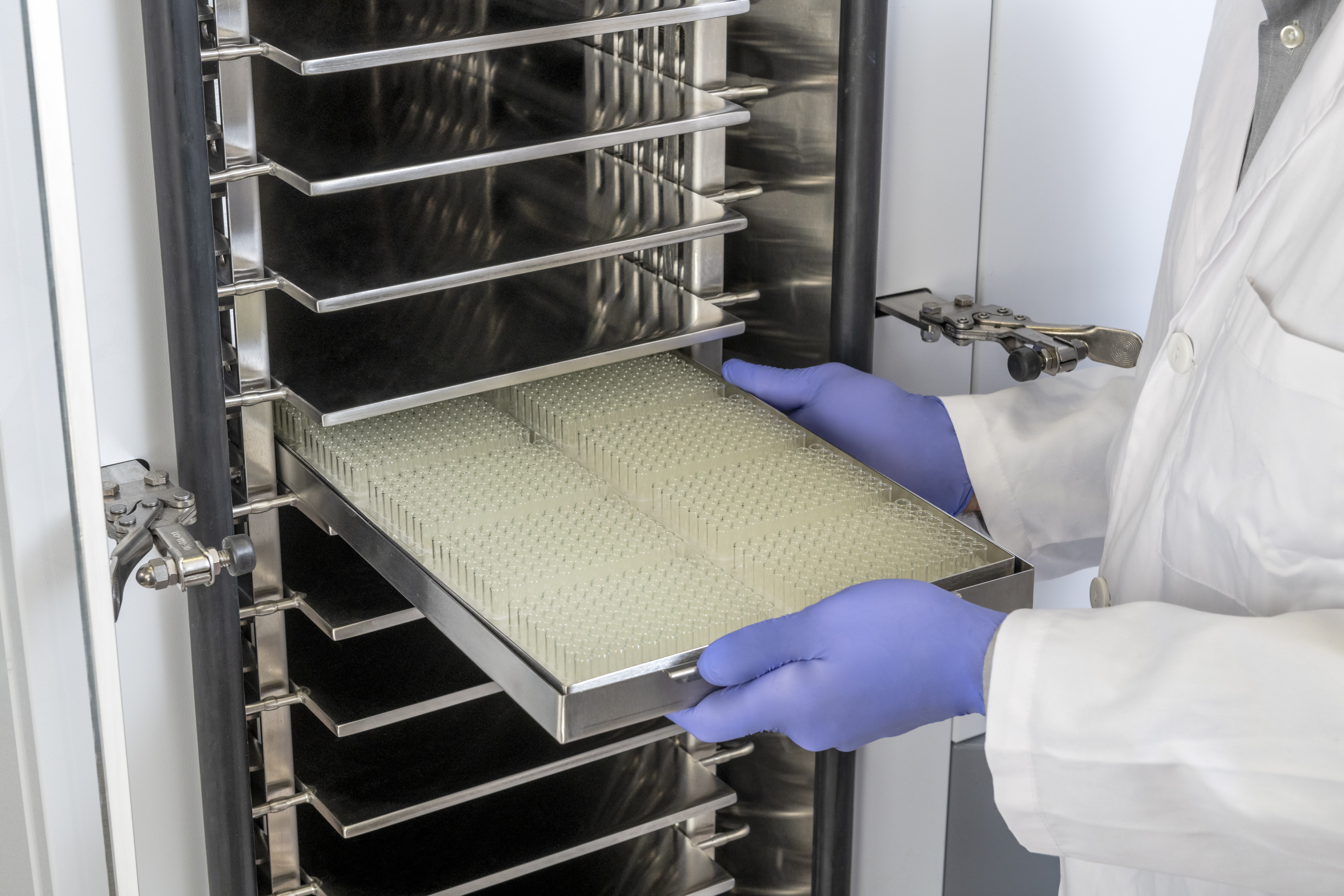 A scientist putting a tray of vial into a freeze dryer.